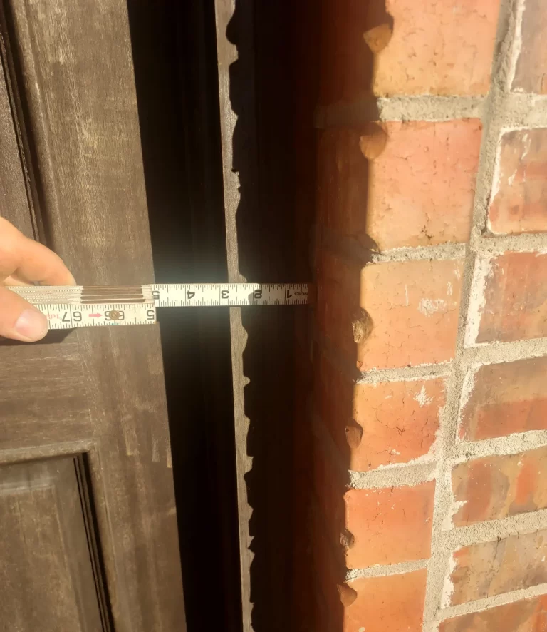 Tape measure showing a wide gap between an exterior door and its brick frame