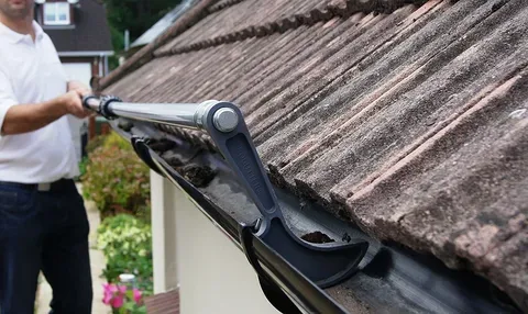 Homeowner clearing debris from a roof gutter with an extension tool