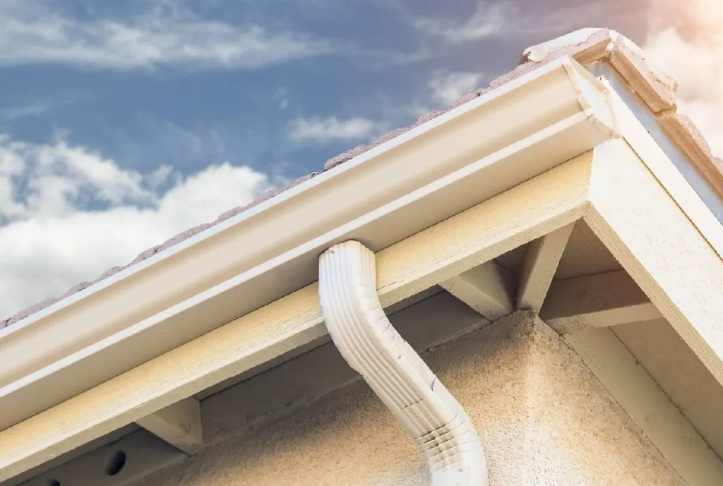 Technician on a ladder repairing and re-pitching a white residential gutter run