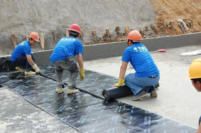 Technician applying waterproofing membrane to an excavated foundation wall